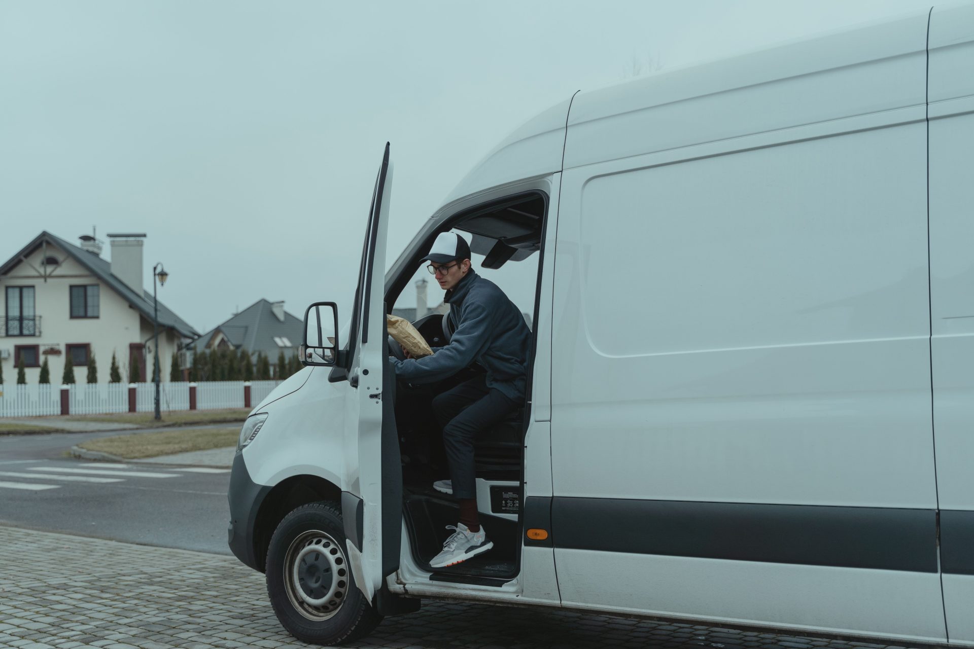Ein Kurier liefert ein Paket aus einem Lieferwagen in einem Wohngebiet aus – eine Darstellung von Logistik und Zustelldiensten auf der „letzten Meile“.
