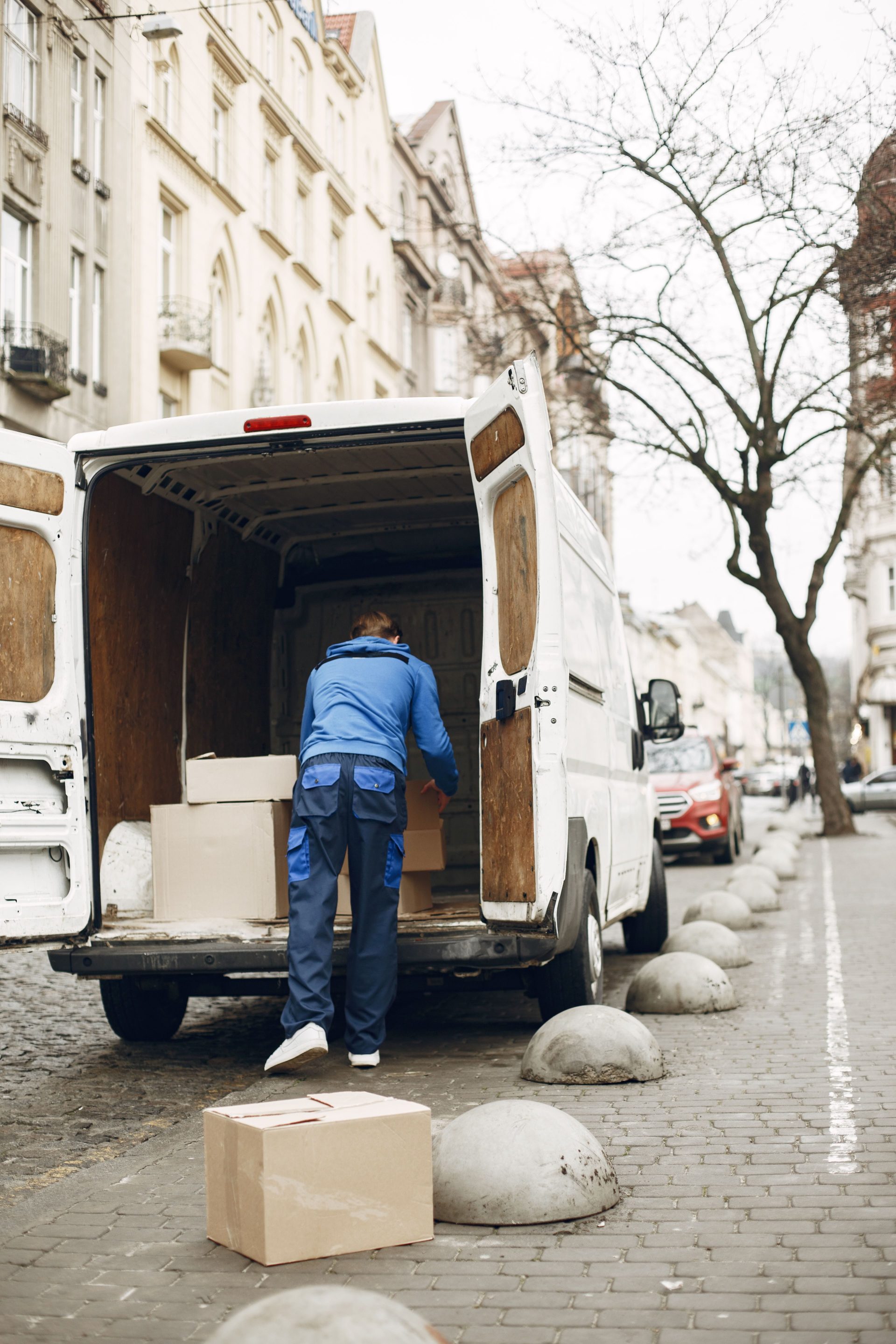 Ein Lieferbote lädt auf einer belebten Stadtstraße Pakete in einen Transporter und veranschaulicht so die städtische Logistik.