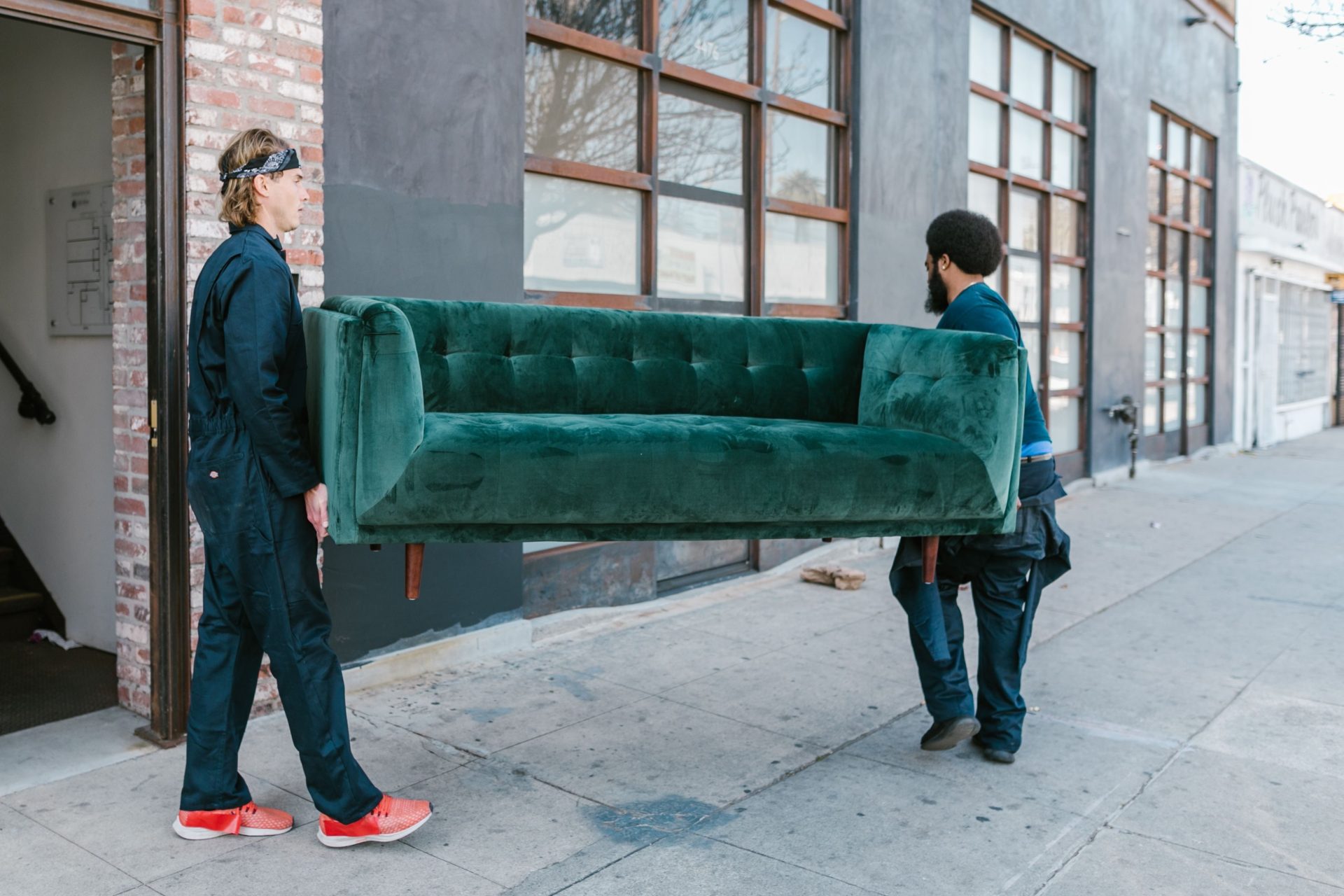 Zwei Männer tragen ein grünes Sofa auf einer Straße in der Stadt – ein Beispiel für Teamarbeit und Umzugsdienstleistungen.