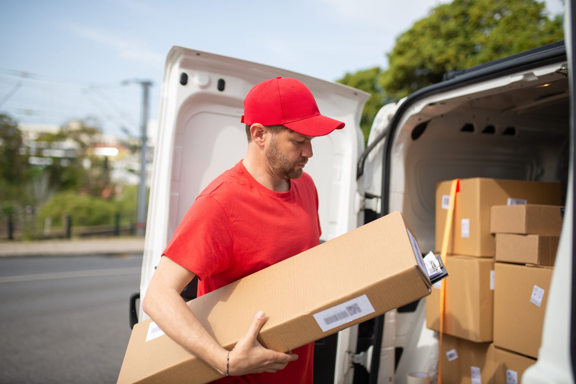 Ein Kurier in roter Uniform lädt an einem sonnigen Tag Pakete aus einem Lieferwagen.