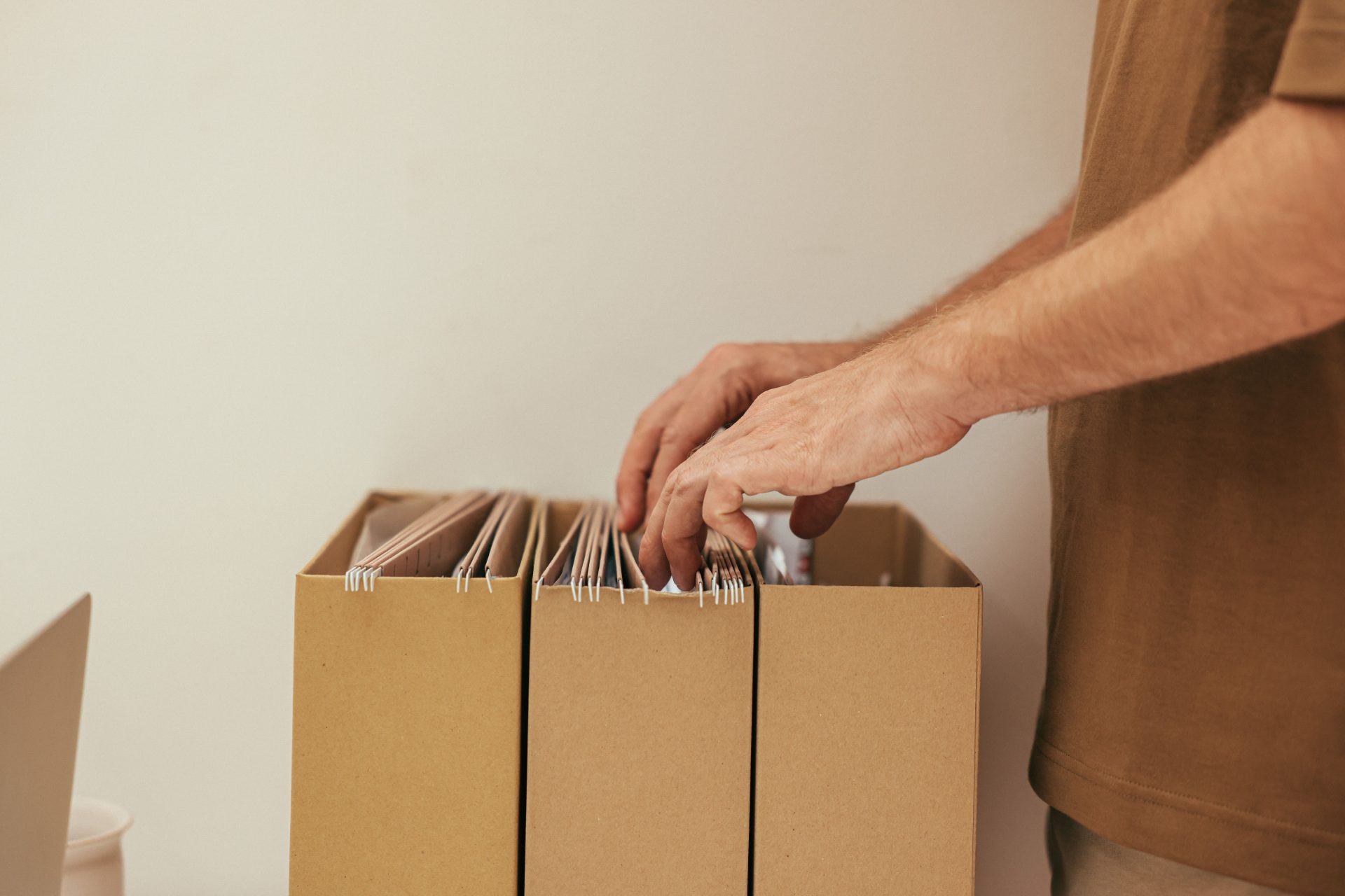 Nahaufnahme einer Person, die Unterlagen in Pappkartons ordnet – ideal für Themen aus den Bereichen Wirtschaft und Büro.